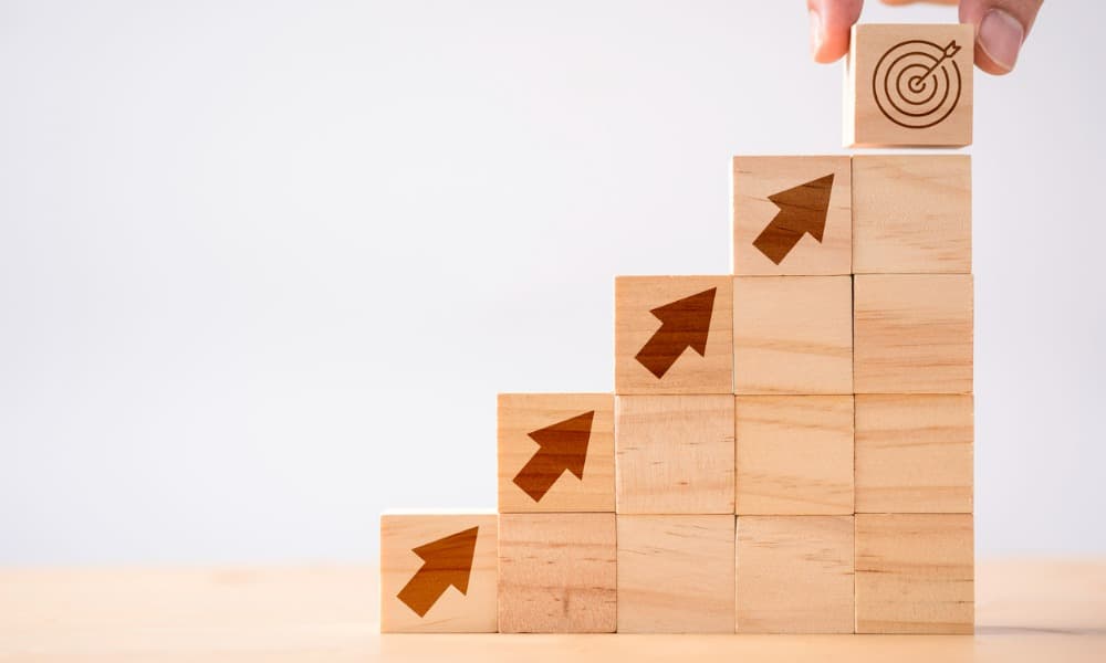 A hand putting a bullseye at the top of a stock of boxes with arrows indicating the stages of vertical development.